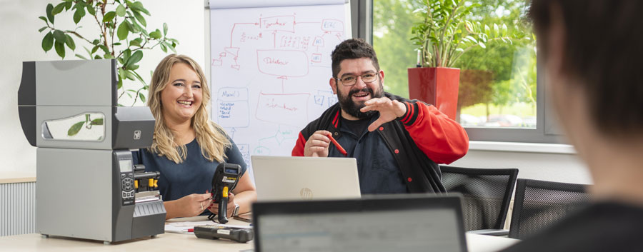 Das Bild zeigt eine SAP-Entwicklerin und einen SAP-Entwickler, die gemeinsam eine Systemlösung zur mobilen Datenerfassung in der Logistik vorstellen.