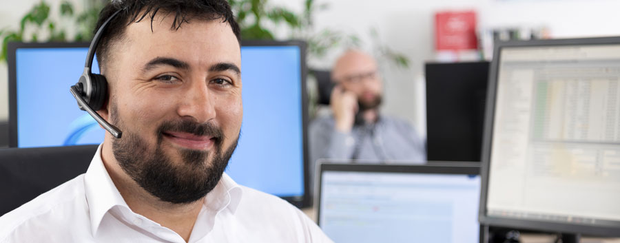 Auf diesem Bild ist ein Supportmitarbeiter von prismat porträtiert. Im Hintergrund sind Bildschirme mit verschiedenen Übersichten.